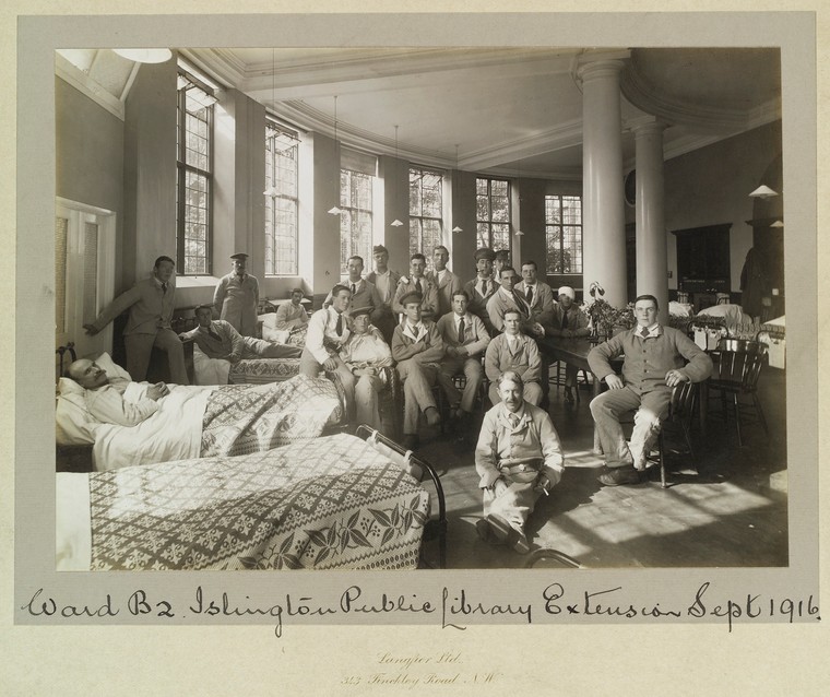 An old photography displaying men in a variet of uniforms posing, some on beds. The caption reads " Ward B2 Islington Public Library Extension Sept 1916"